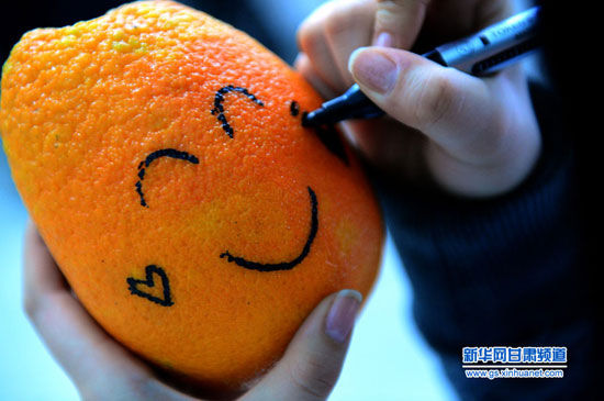12月26日,兰州大学达尔文协会的一名志愿者在橙子上绘制笑脸图案.